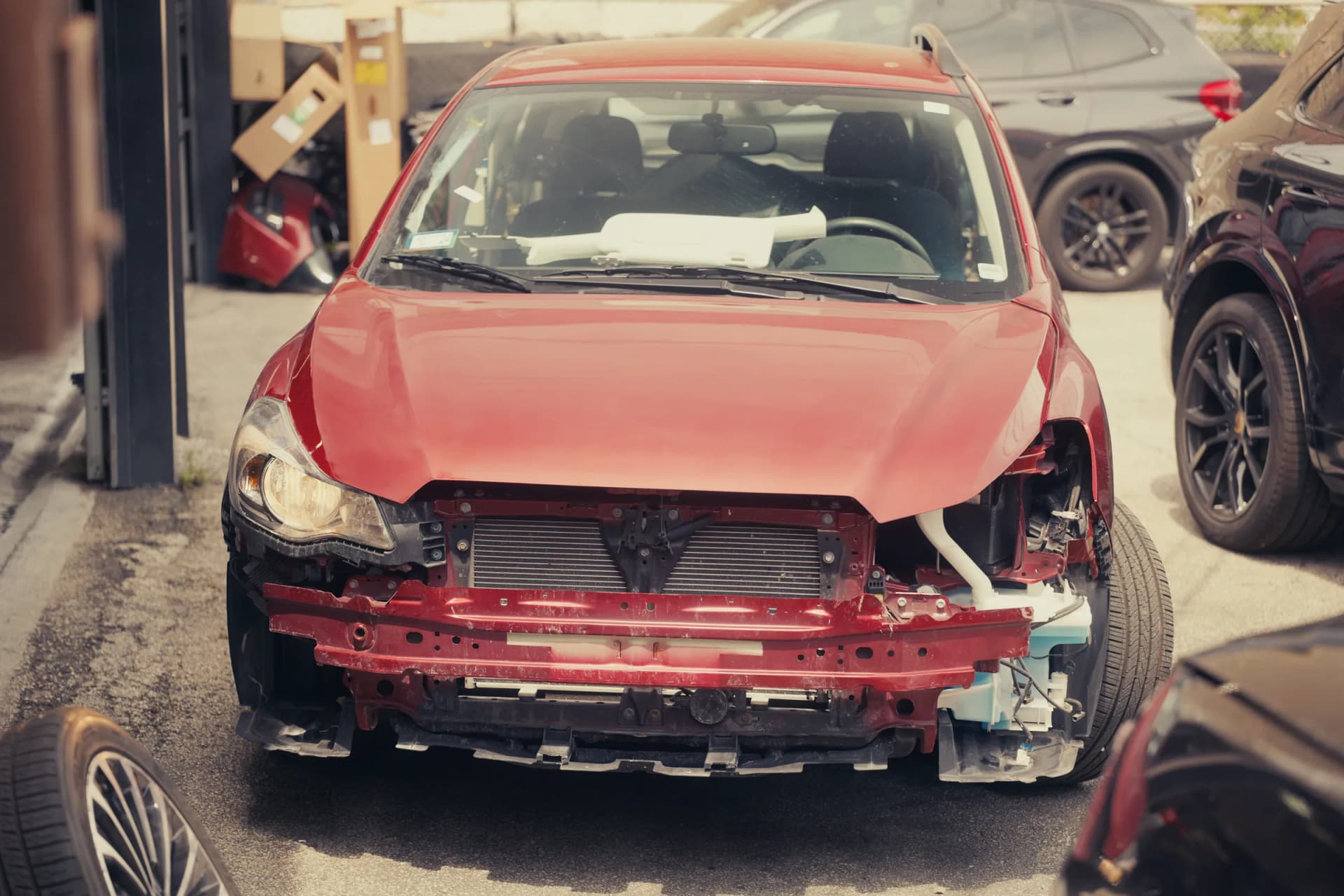 Front-end collision damage on a red sedan awaiting body repair at Carrectly