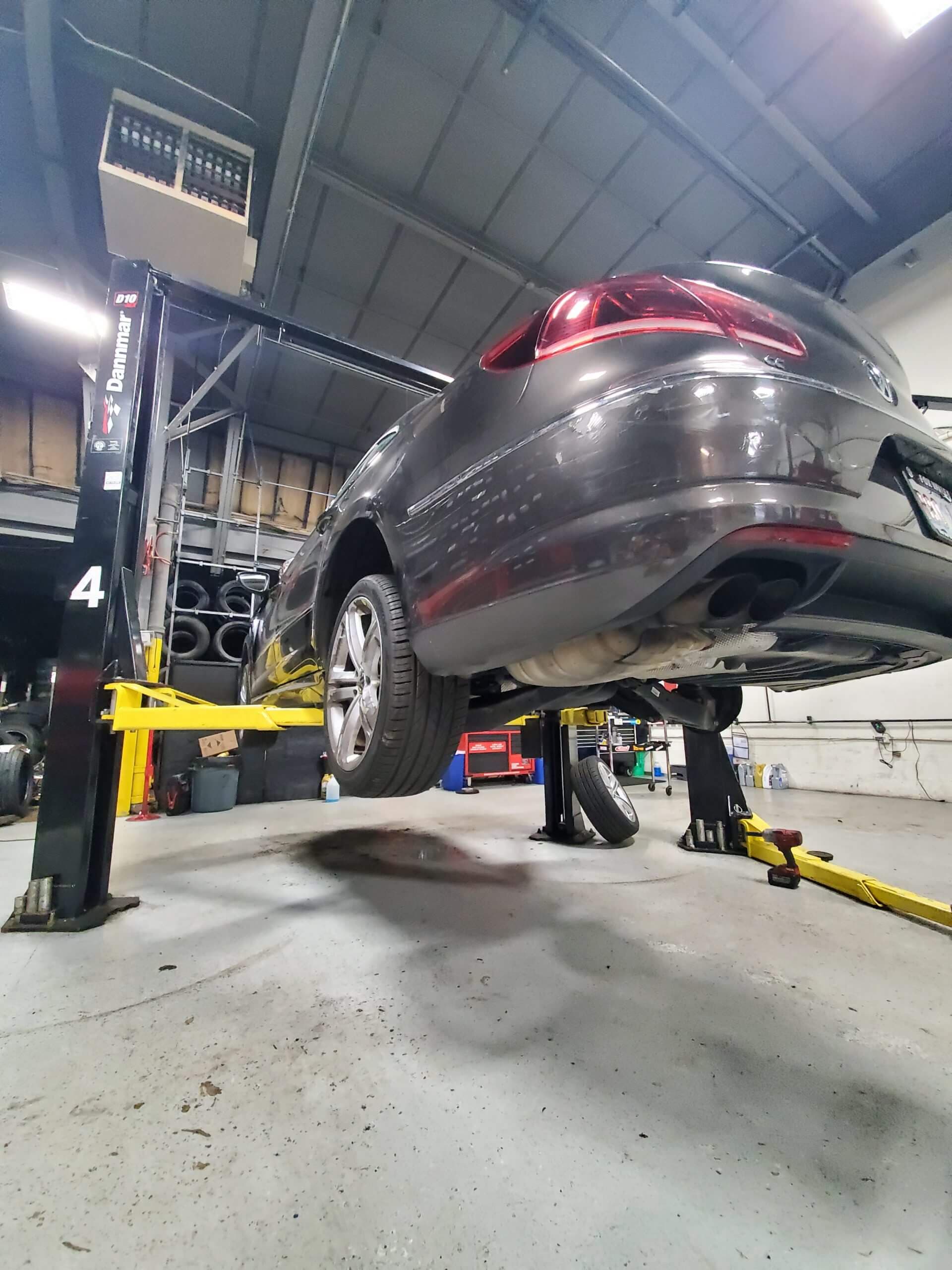 Dark sedan lifted in a garage, undergoing brake pads replacement
